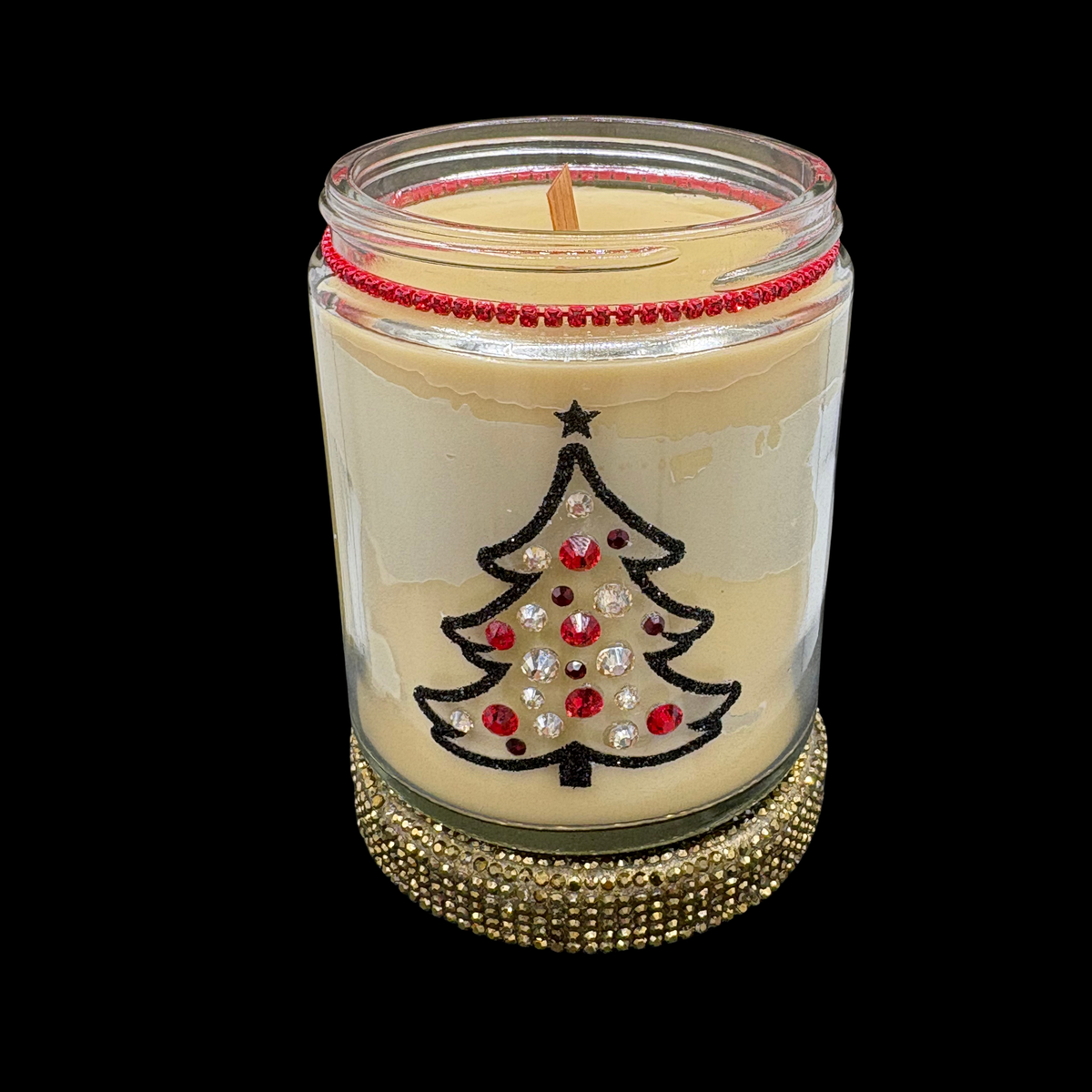 A holiday-themed jar candle with cream-colored wax, featuring an embroidered black Christmas tree adorned with red, silver, and clear rhinestones, a red beaded rim, and a gold rhinestone-embellished base, set against a solid black background.