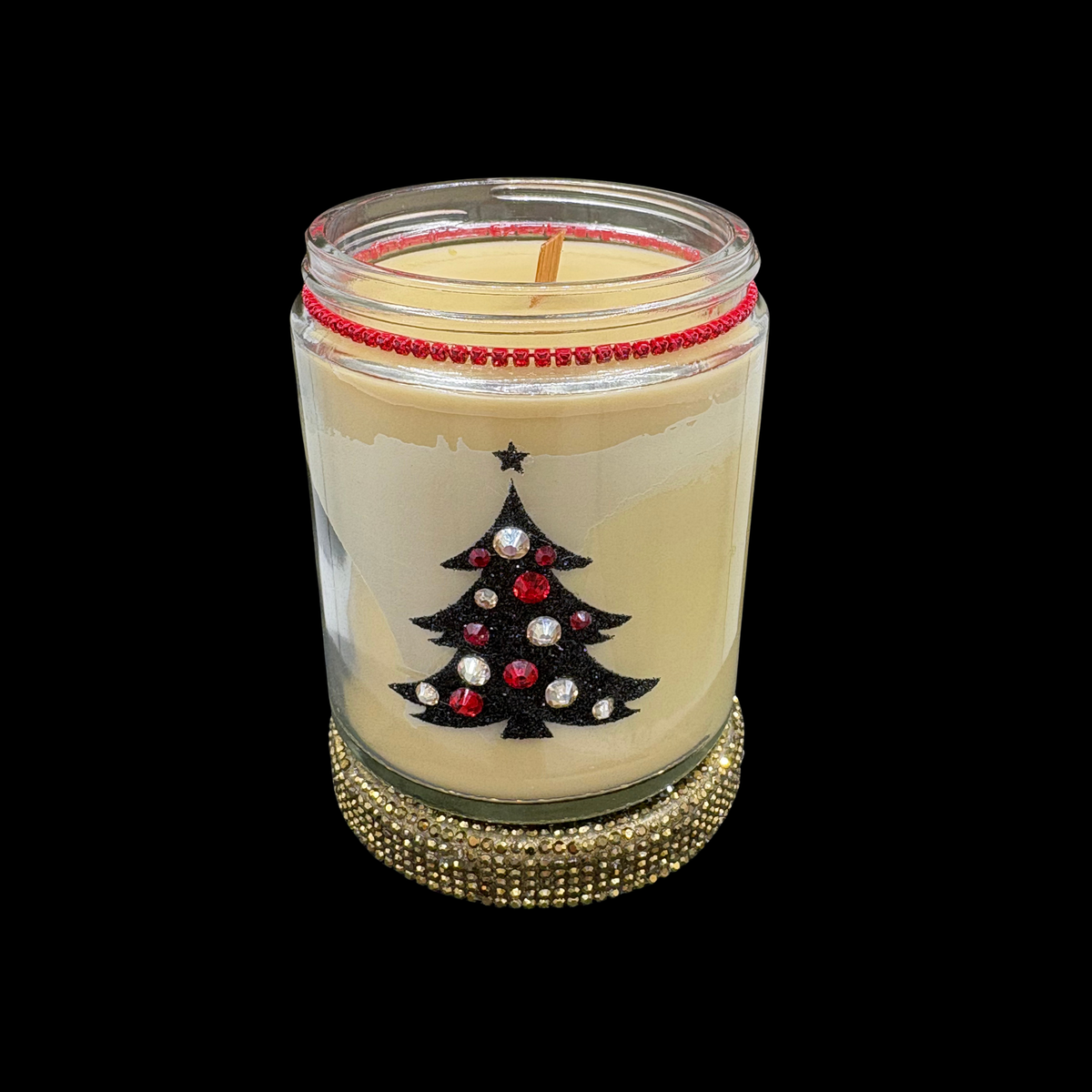 A holiday-themed candle in a clear glass jar with cream-colored wax, featuring a black glitter Christmas tree with red and silver rhinestone ornaments on the front. The jar is decorated with a red beaded rim and sits on a gold rhinestone-covered base, set against a solid black background.