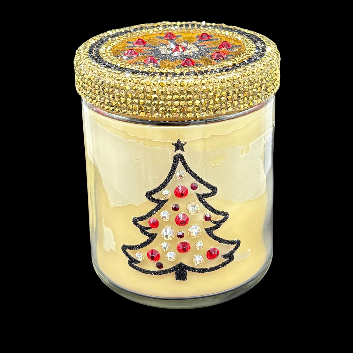 A clear glass jar candle with pale yellow wax, featuring a black glitter Christmas tree design on the front embellished with red and clear rhinestones, and a gold rhinestone-encrusted lid, shown against a solid black background.
