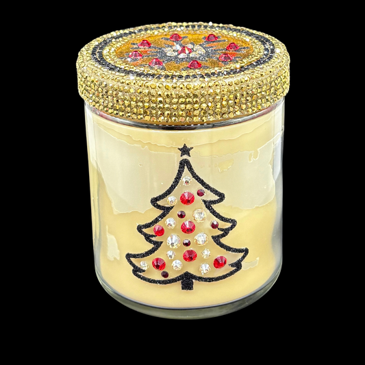 A clear glass jar candle with pale yellow wax, featuring a black glitter Christmas tree design on the front embellished with red and clear rhinestones, and a gold rhinestone-encrusted lid, shown against a solid black background.