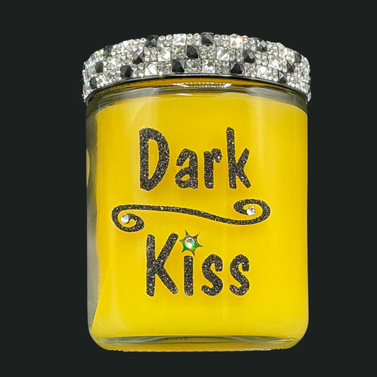 Yellow candle jar with 'Dark Kiss' text and decorative lid on a black background
