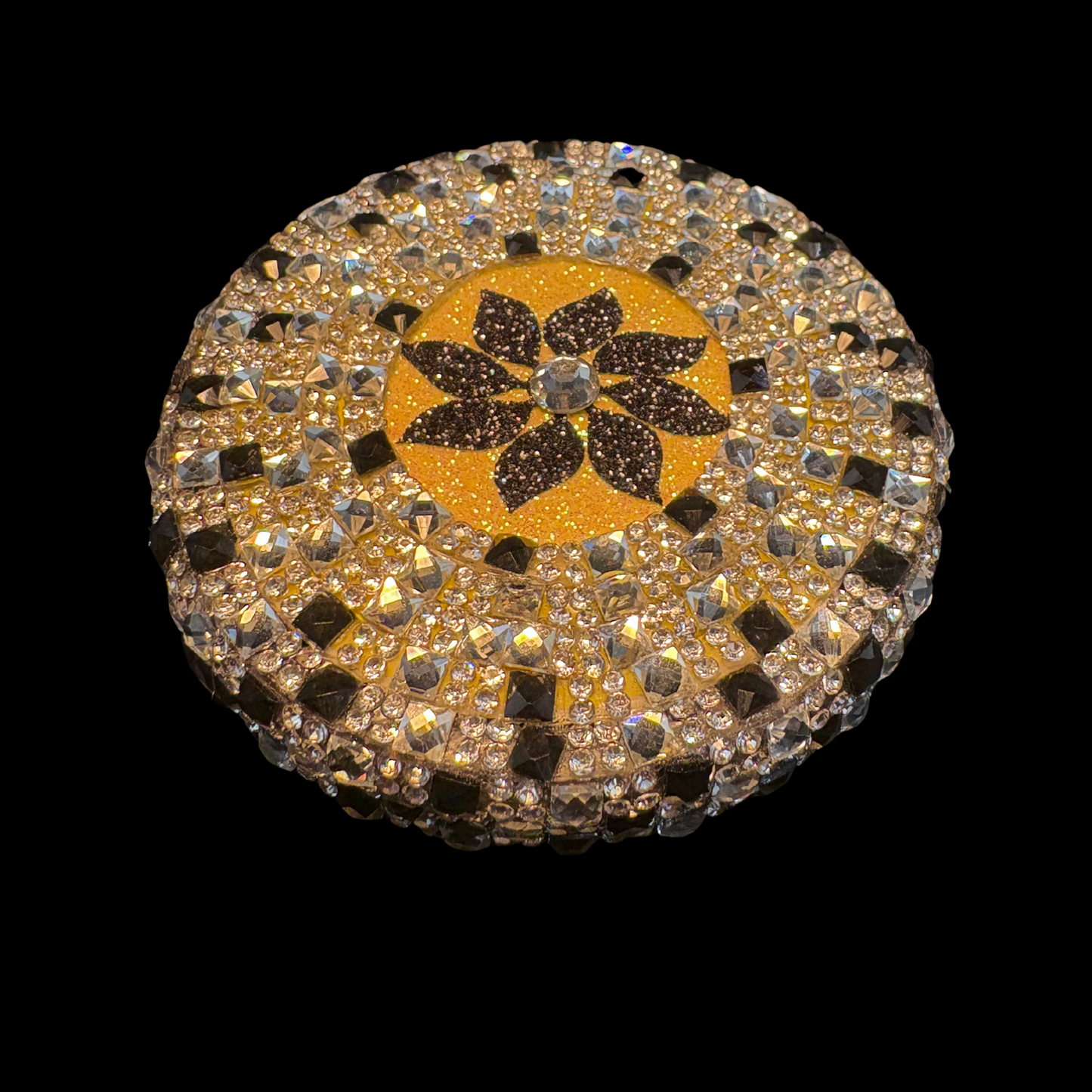 Round decorative item with a floral design and rhinestones on a black background