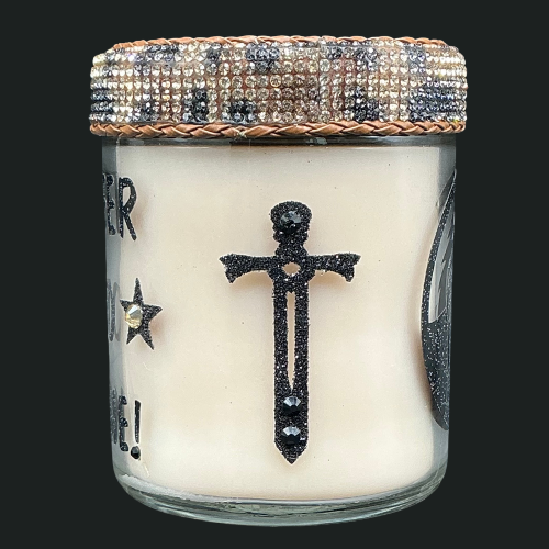 Candle in a glass jar with decorative cross and star design on a black background