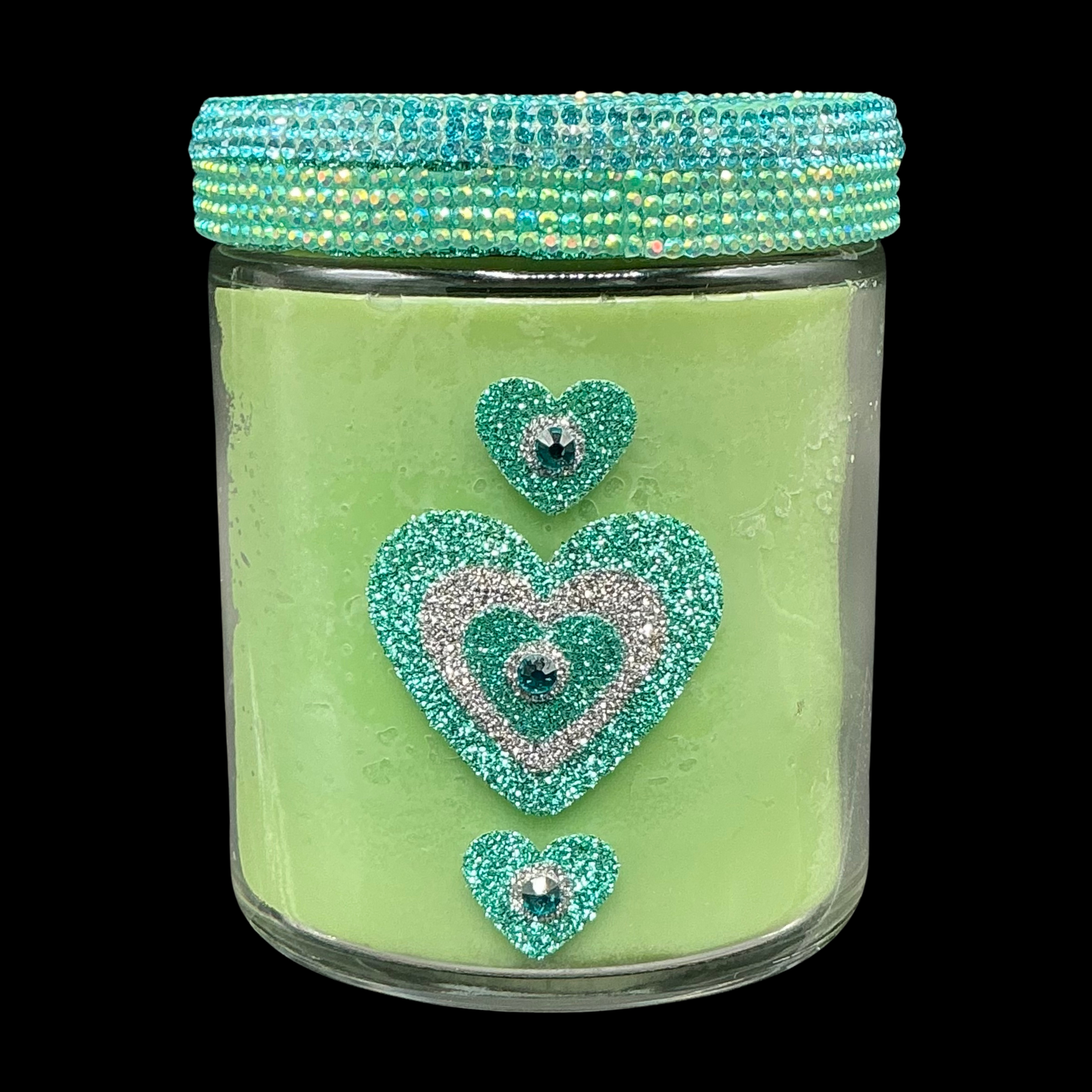 Decorative glass jar with green candle, turquoise lid, and heart-shaped designs on a black background