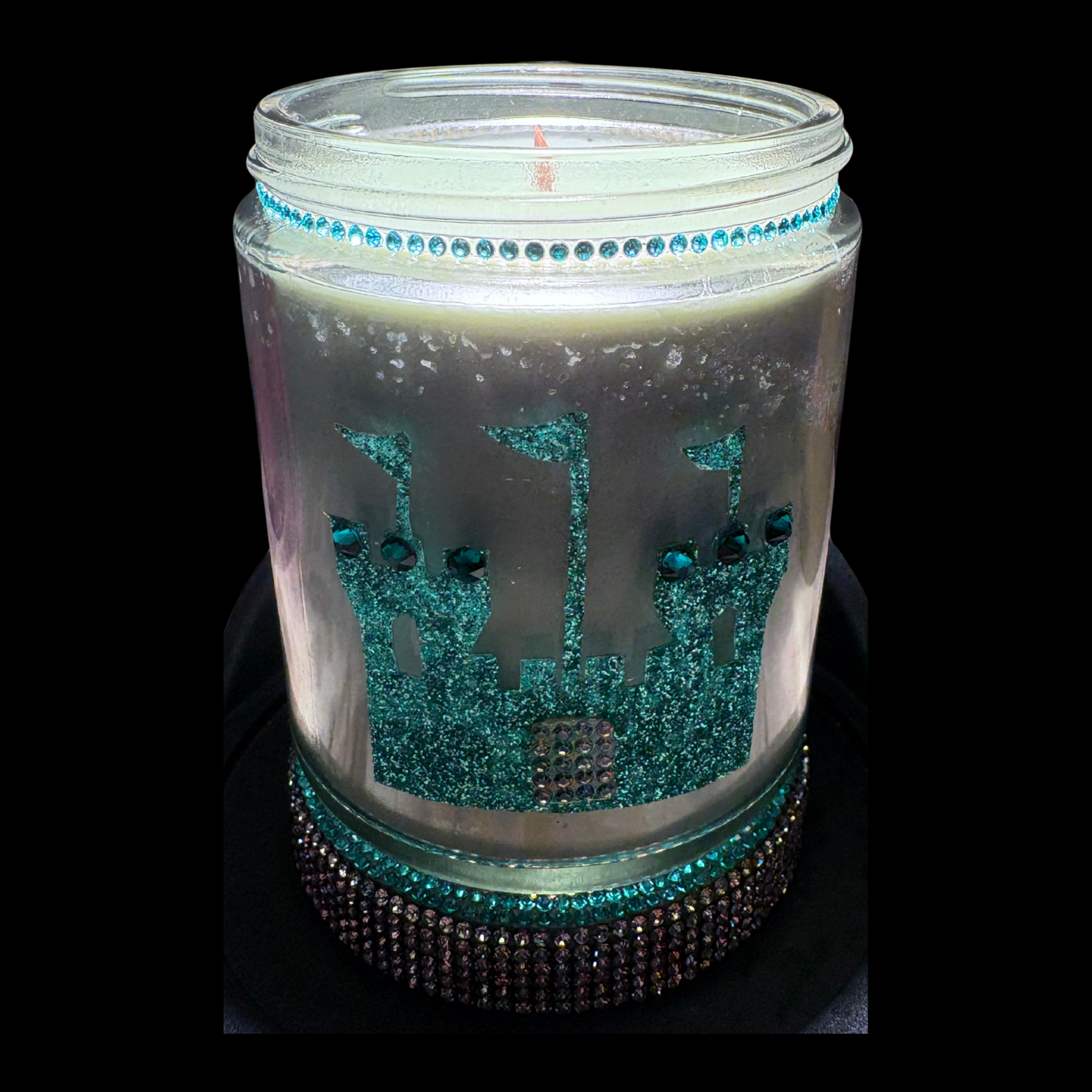 Decorative candle with castle design and turquoise embellishments on a black background