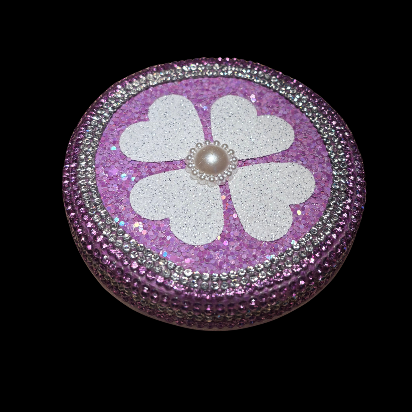 Decorative purple round object with a white flower and pearl center on a black background