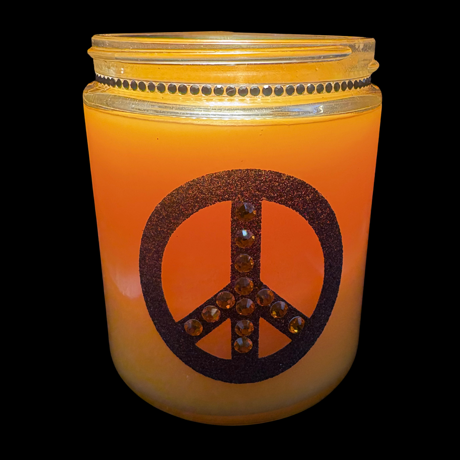 Orange candle in a jar with a peace symbol design on a black background