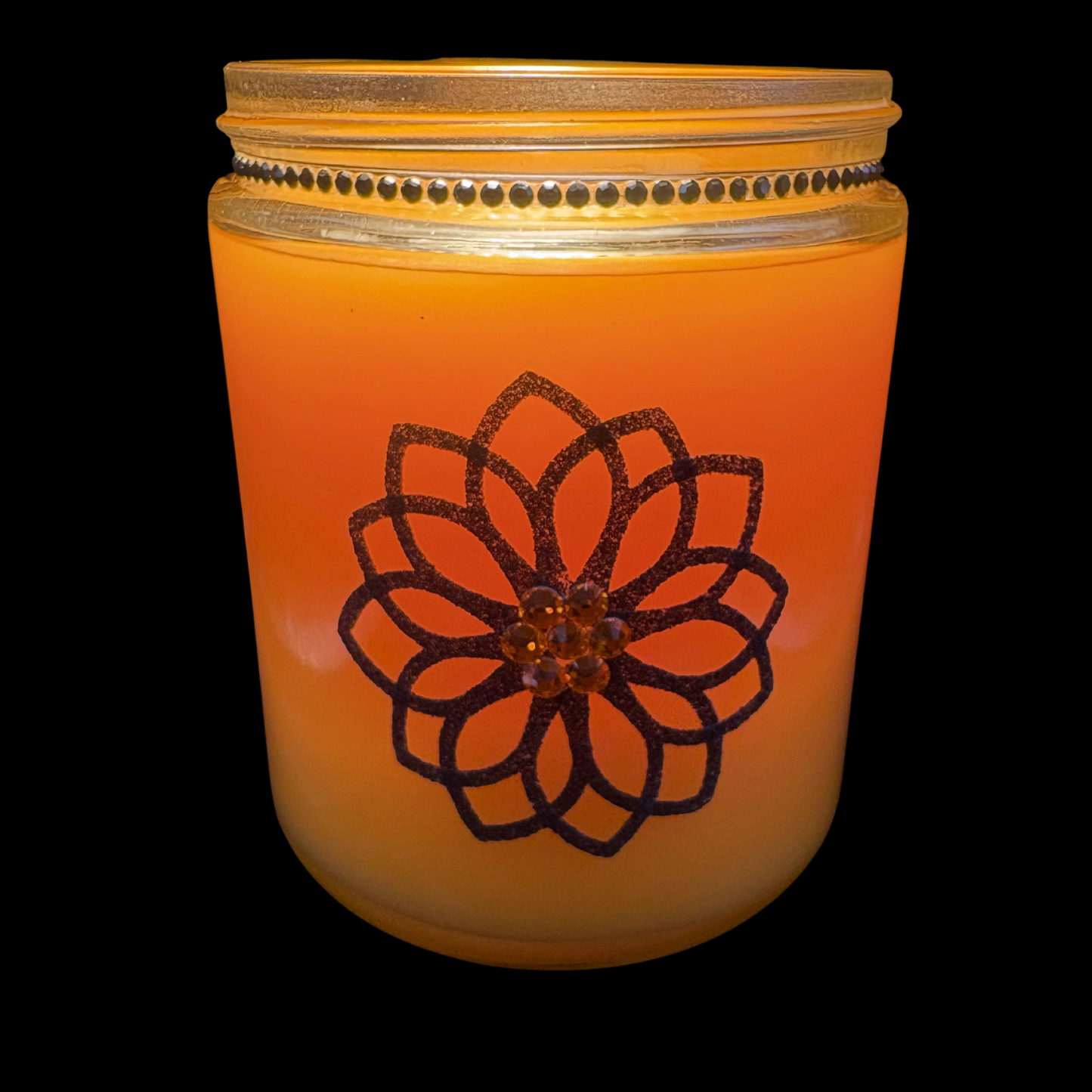 Orange candle in a glass jar with a decorative black flower design on a black background