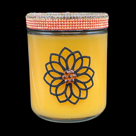 Yellow candle with a decorative flower design and beaded lid on a black background