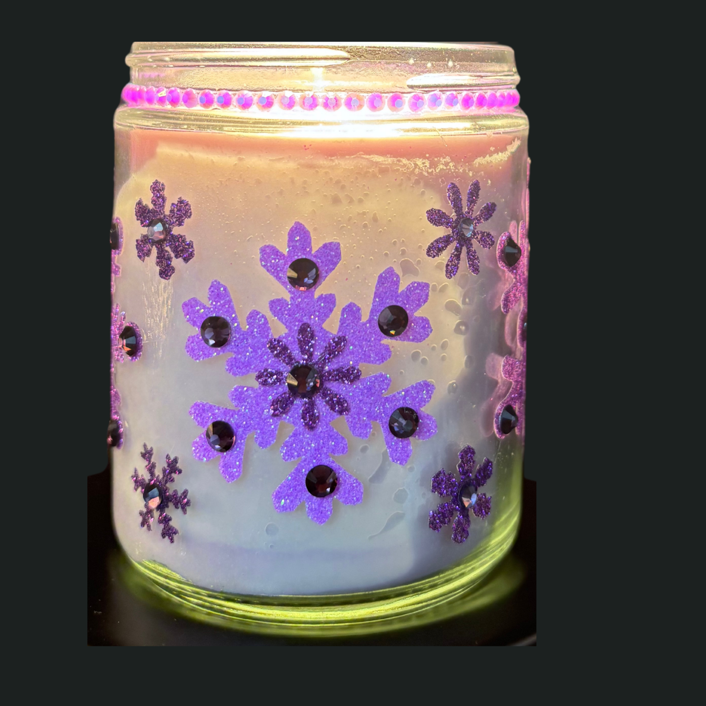 Candle in a jar with purple snowflake designs on a black background