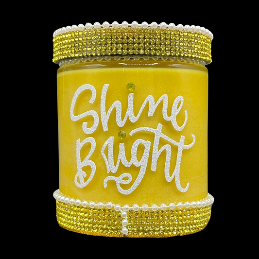 Yellow candle jar with 'Shine Bright' text and decorative lid on a black background