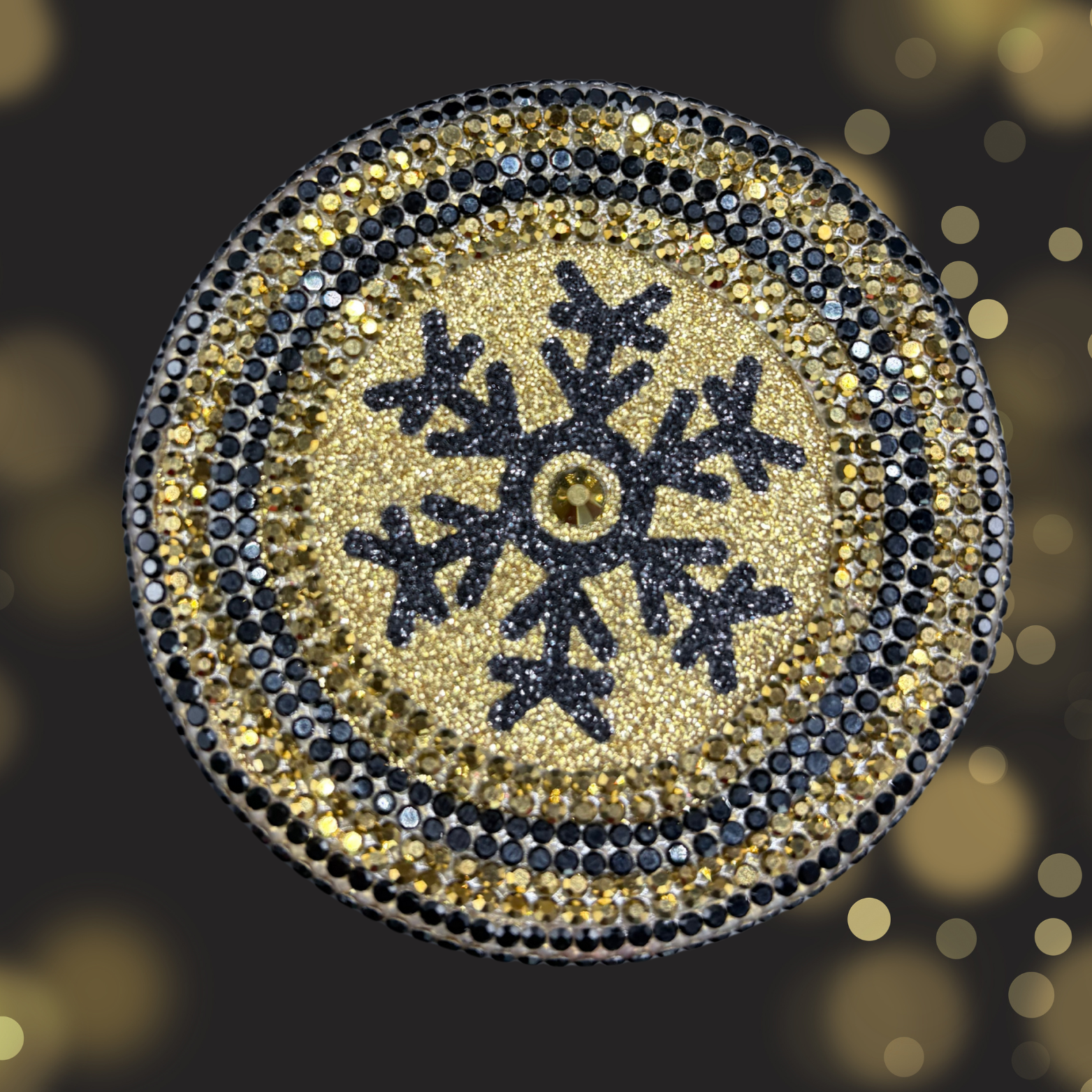 Decorative button with a snowflake design and gold and black color scheme on a blurred background.