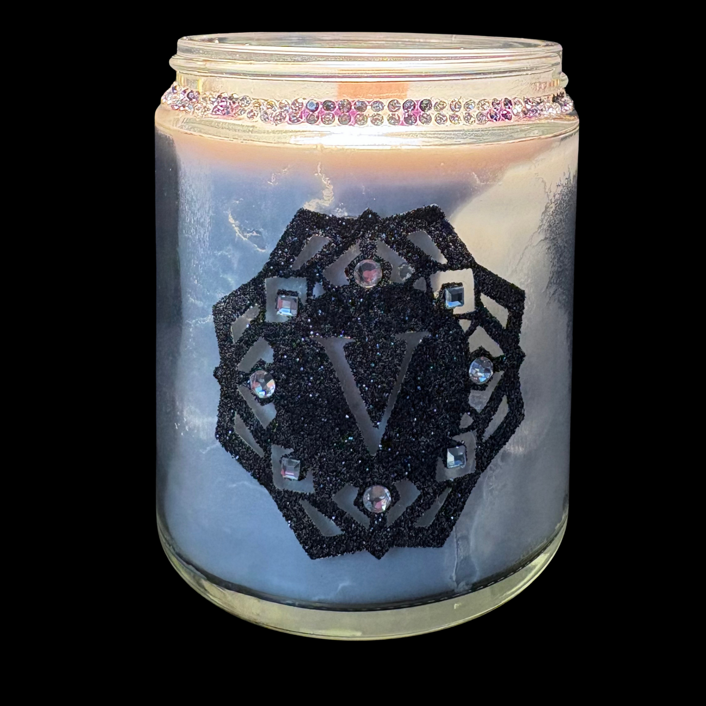 Candle in a glass jar with decorative emblem and rhinestones on a black background