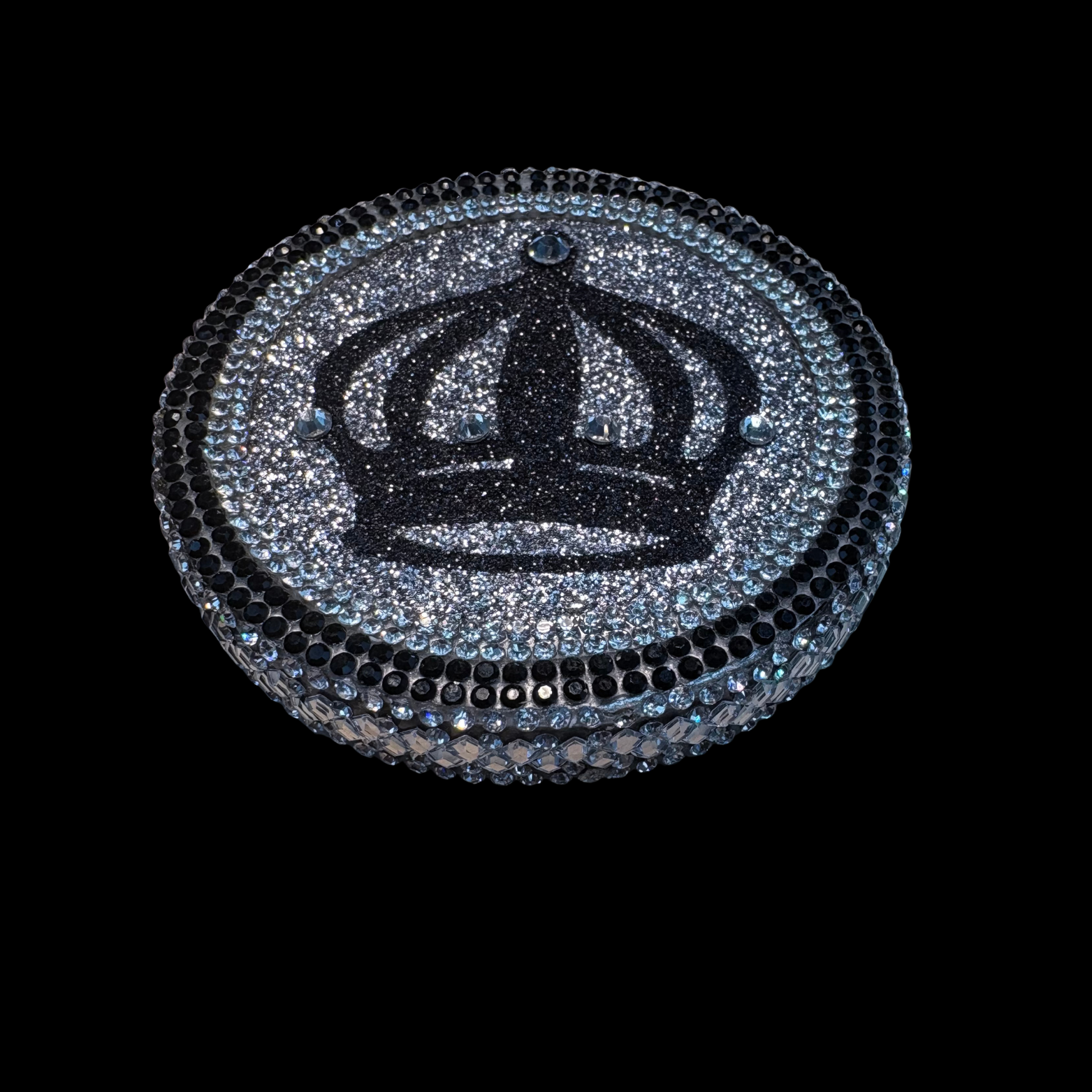 Decorative item with a black crown design on a round, glittery surface against a black background