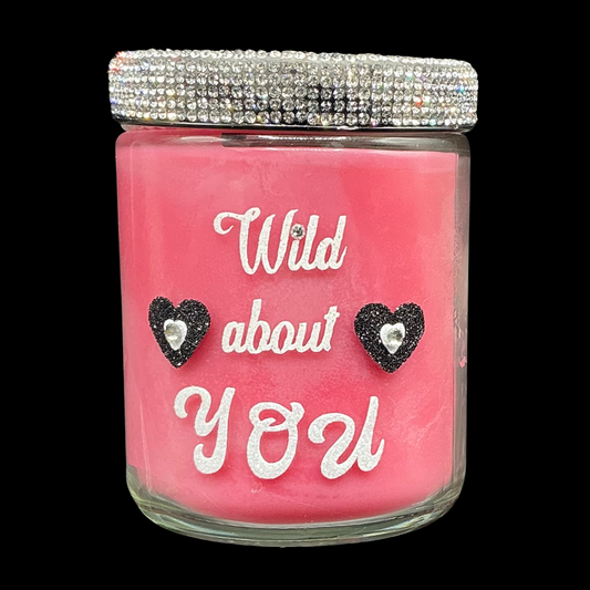 Pink candle jar with 'Wild about You' text and heart-shaped earrings on a black background